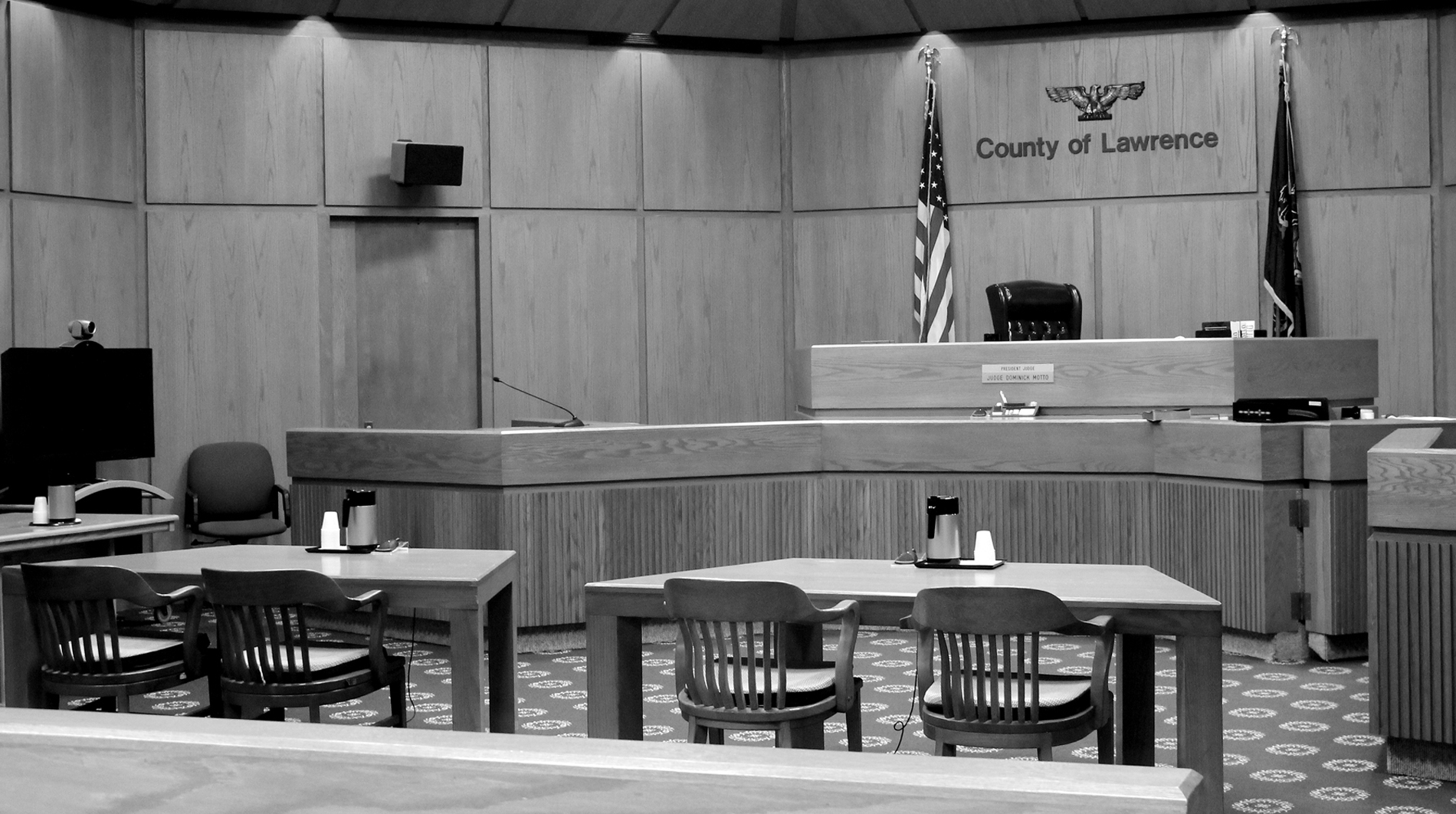 The courtroom of Judge Motto, at the Lawrence County Courthouse, the defendants and plantiffs tables and chairs sit in the foreground and the judges desk sits at the front of the wood paneled room.