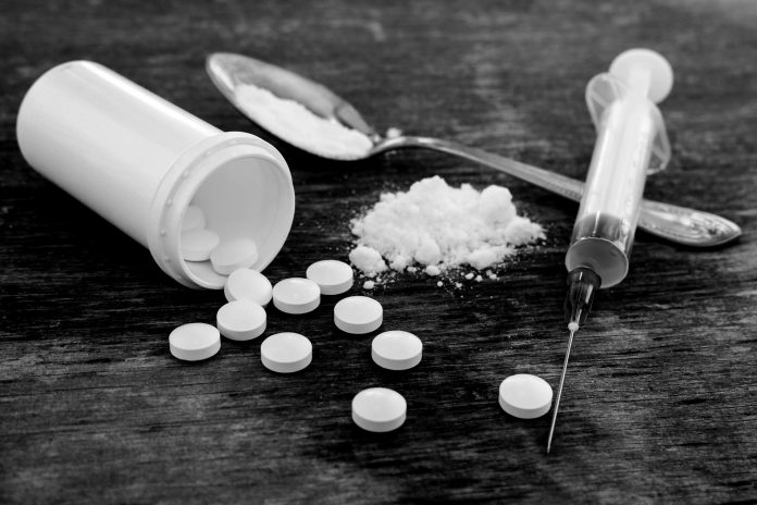 Pills, Fentynal Powder, and Heroin syringe sit on a table