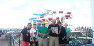 The Swartz family and friends stand on the deck of their cruise ship with the waterslides in the background and a Farm and Dairy in their hands.