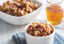 Honey Roasted Bridge Mix A small bowl of Honey roasted bridge mix, sits on top of a blue napkin with a larger bowl of the mix and a glass jar of hone in the background.