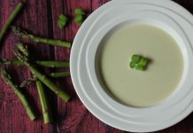 Cream of Asparagus Soup A bowl of light green soup with slices of asparagus in the center and shots on the table beside the bowl
