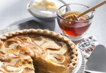 Honey Cream Pumpkin Pie A Honey Cream Pumpkin Pie sits with one piece taken out of it. Two glass bowls, one filled with honey, the other filled with whipped cream, sit in the background of the image.