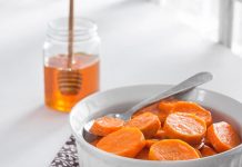 Candied Yams Candied Yams in a white serving dish with a glass honey container and dipper behind it.