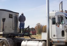 Farmers unite to help neighbor harvest A farmer stands on a semi truck, watching combines harvest.