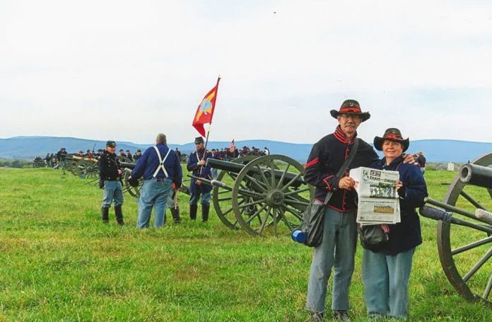 The Dazeys stand dressed in Union soldier uniforms on the battle field. A group of Union soldiers stand behind them near an Civil War era cannon.