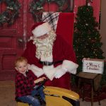 Santa visits dairy farm for milk and cookies A child sits on a yellow toy tractor in front of Santa.