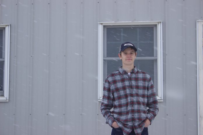 Michael Baer, 18, stands in front of a barn at Rogers Community Auction while it snows.