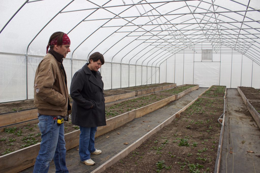 A man and a woman stand next to a raised growing bed in a high tunnel.