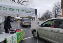 Farmers markets adjust to COVID-19 social distancing guidelines A man stands under a tent at a farmers market and talks to a woman in her car.