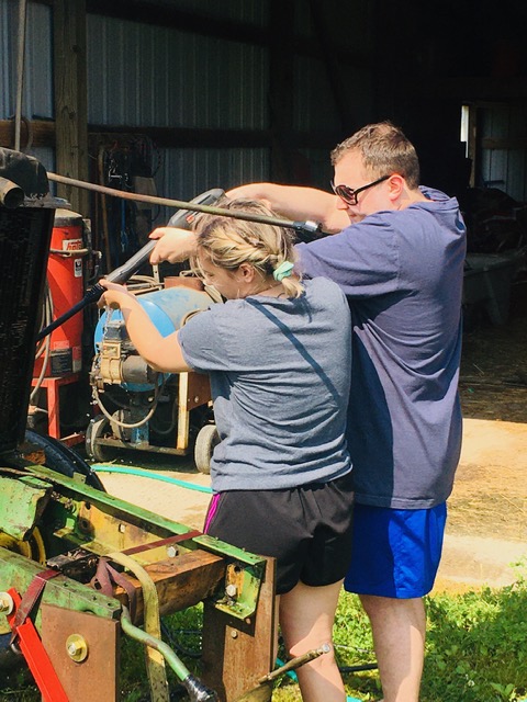 A man and a woman pressure wash part of a tractor.