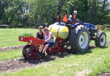 Ohio farmers get started on first planting season for hemp Two women sit in a vegetable planter while a man drives the tractor attached to it.