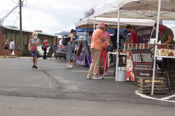 Customers walk around stands at a farmers market.