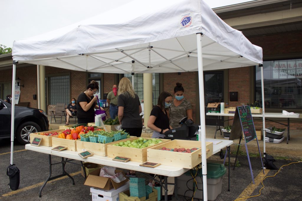 People work at a stand for a farmers market.