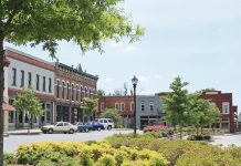 Doing business close to home A small town with cars parked outside the buildings and trees and other greenery in front of it.