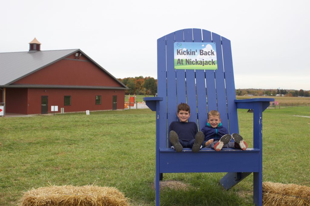 Two boys sit in an oversized chair in front of a barn.