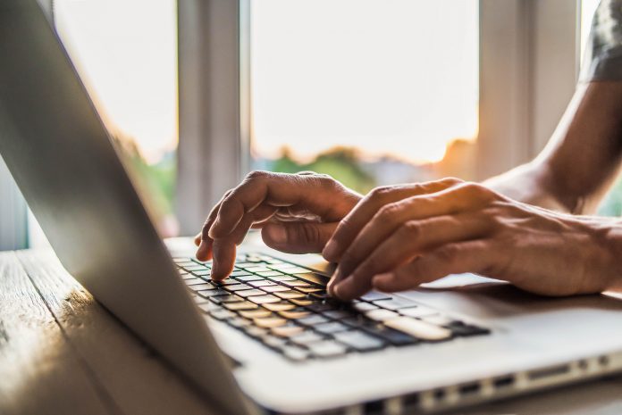 Hands type on a laptop.