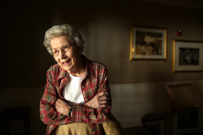 A photo of Mildred Fizer, standing in a room in a red shirt.