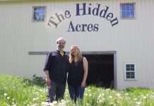 The Hidden Acres balances self-sufficiency with community A man and a woman stand in front of a barn with the words "The Hidden Acres" painted on it.