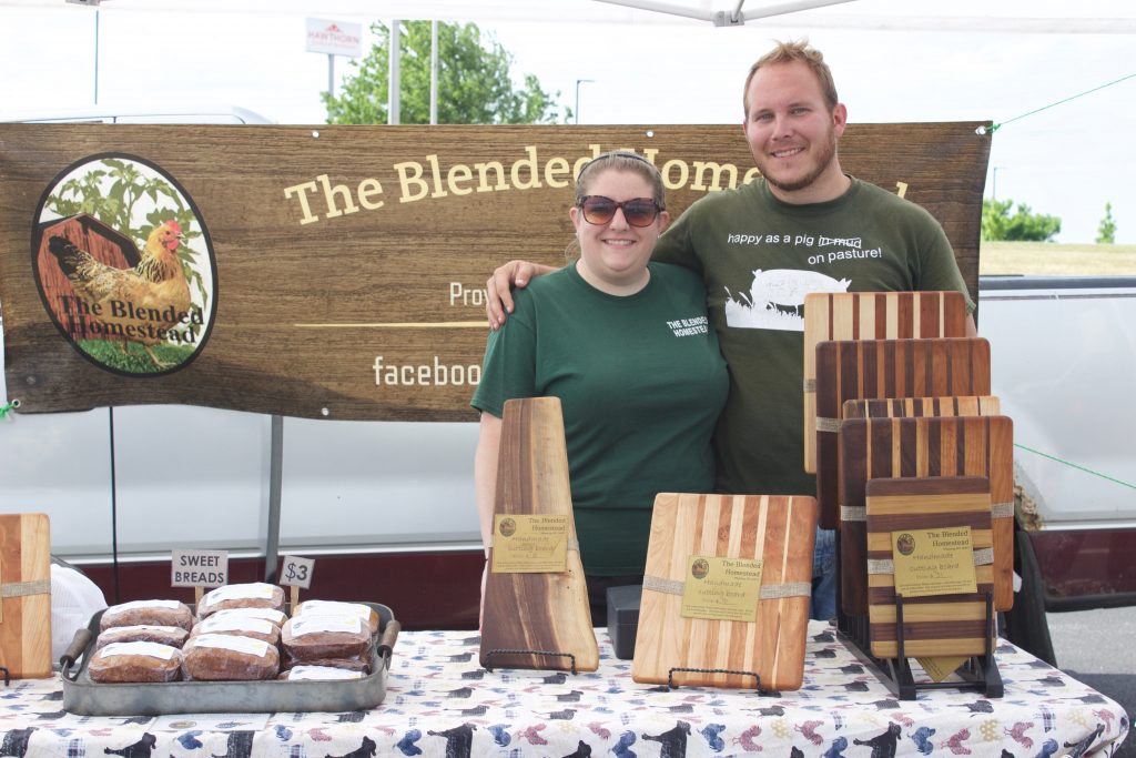 Two farmers stand behind their table at a farmers market.