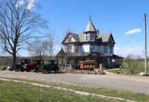 Remembering the good times with the Hawk family antique cars sit outside a victorian home. A home built hearse sits in front of the home with a casket in the back.