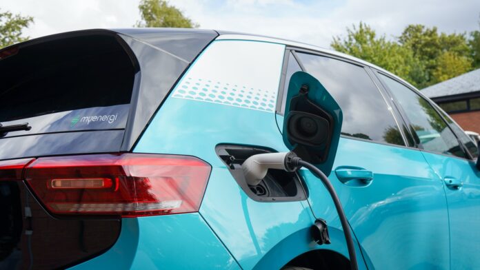 a charging cord is plugged into an electric car behind the rear passenger door