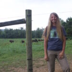 Carie Starr realizes her dream at Cherokee Valley Bison Ranch A woman stands in front of a fence, with bison on the other side.