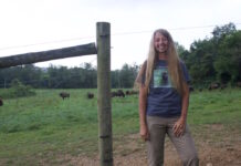 Carie Starr realizes her dream at Cherokee Valley Bison Ranch A woman stands in front of a fence, with bison on the other side.