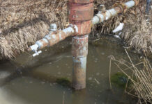 water sits in a trench around a well head casing. the water has bubbles on the surface.