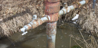 water sits in a trench around a well head casing. the water has bubbles on the surface.
