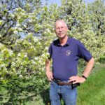 Simmons family moves on from Peace Valley Orchards A white man stand in front of a tree with lots of white flowers on it