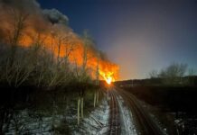 Two sides to every story A flame reaching high into the sky can be seen at the end of a railroad tracks that go up the middle of the photo.