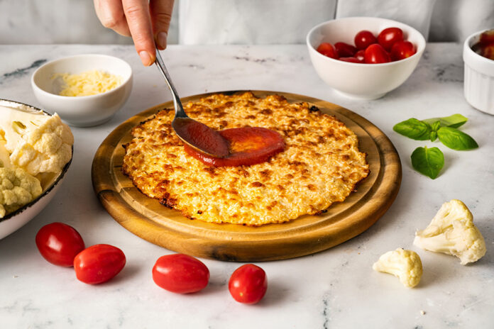 Woman's hands smearing a tomato sauce on the top of cauliflower pizza crust