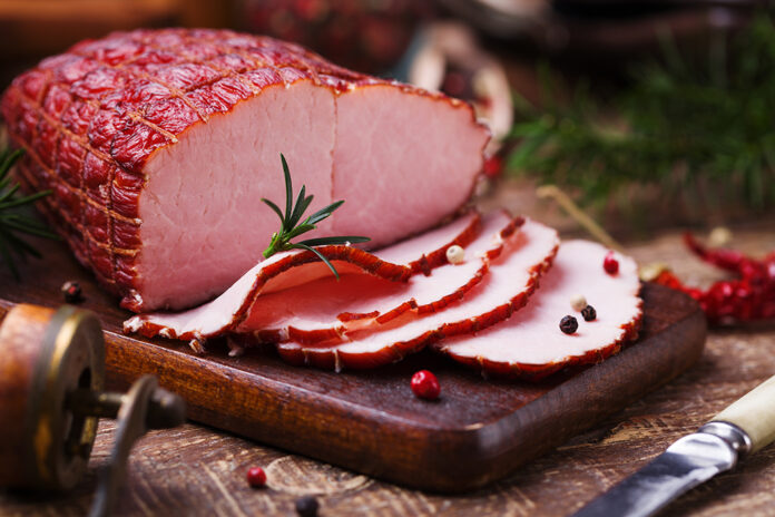 Delicious smoked ham on a wooden board with spices.